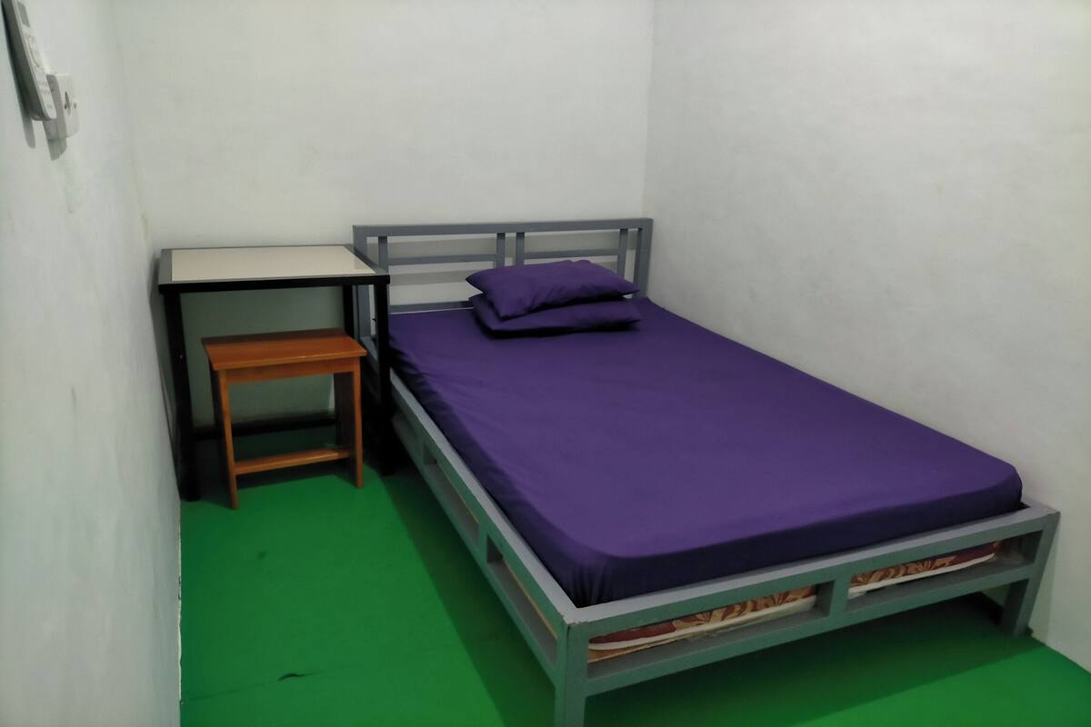 Una habitación pequeña con una cama individual, un colchón morado y una mesita de noche de madera.