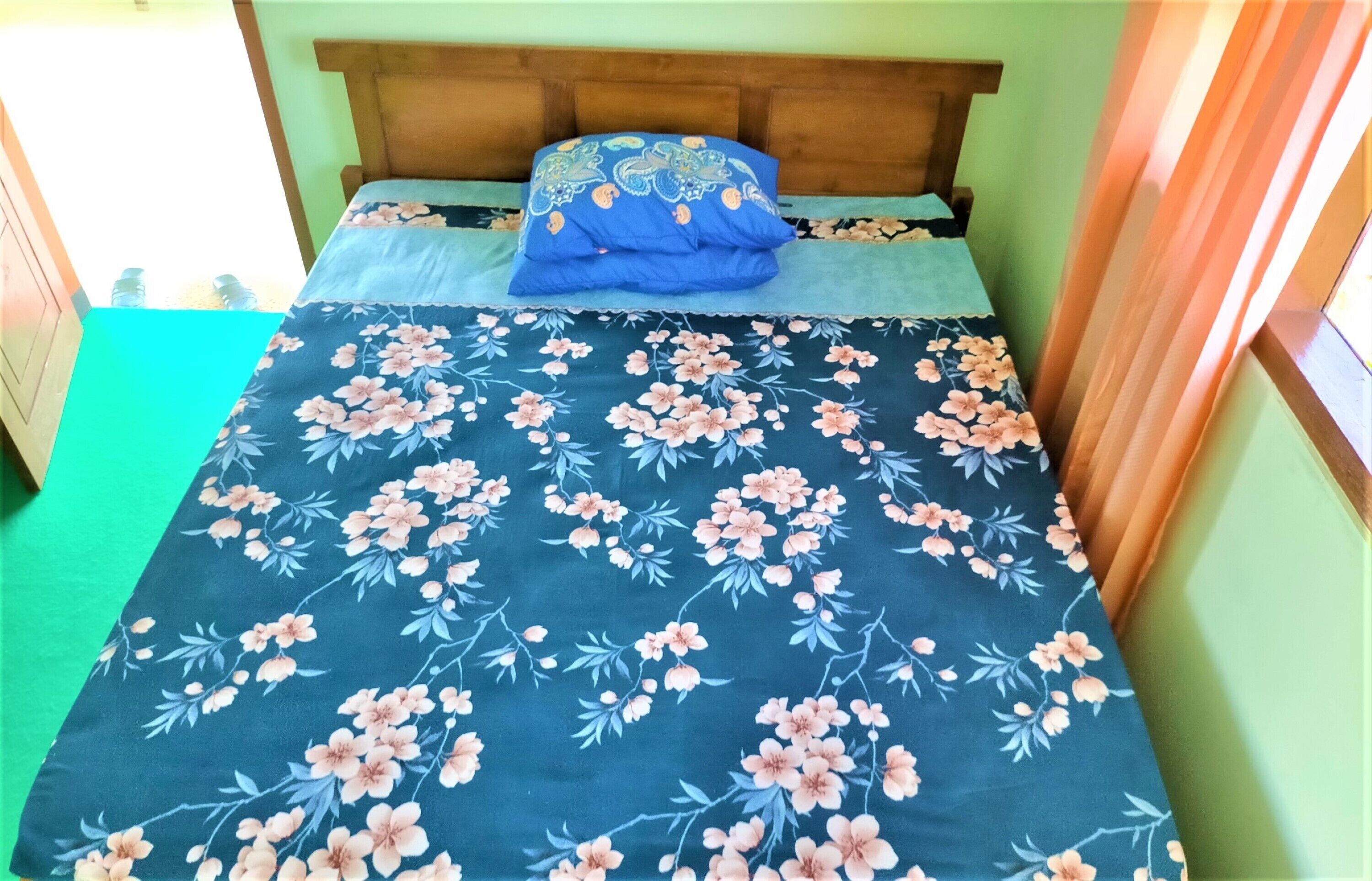 A bed with a floral bedspread, a wooden headboard, and a green floor.