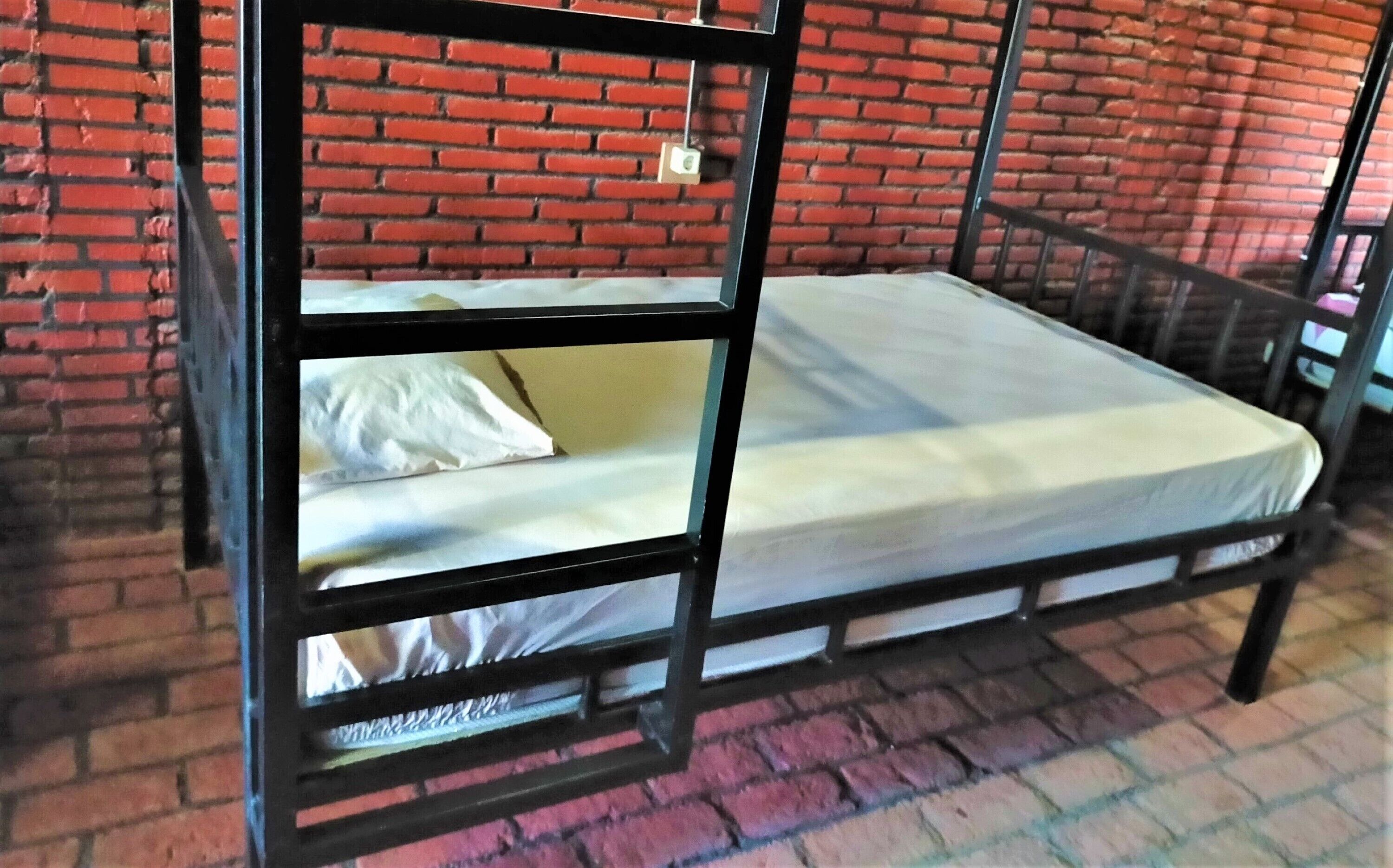 Una cama litera con colchón y almohadas, frente a una pared de ladrillo.