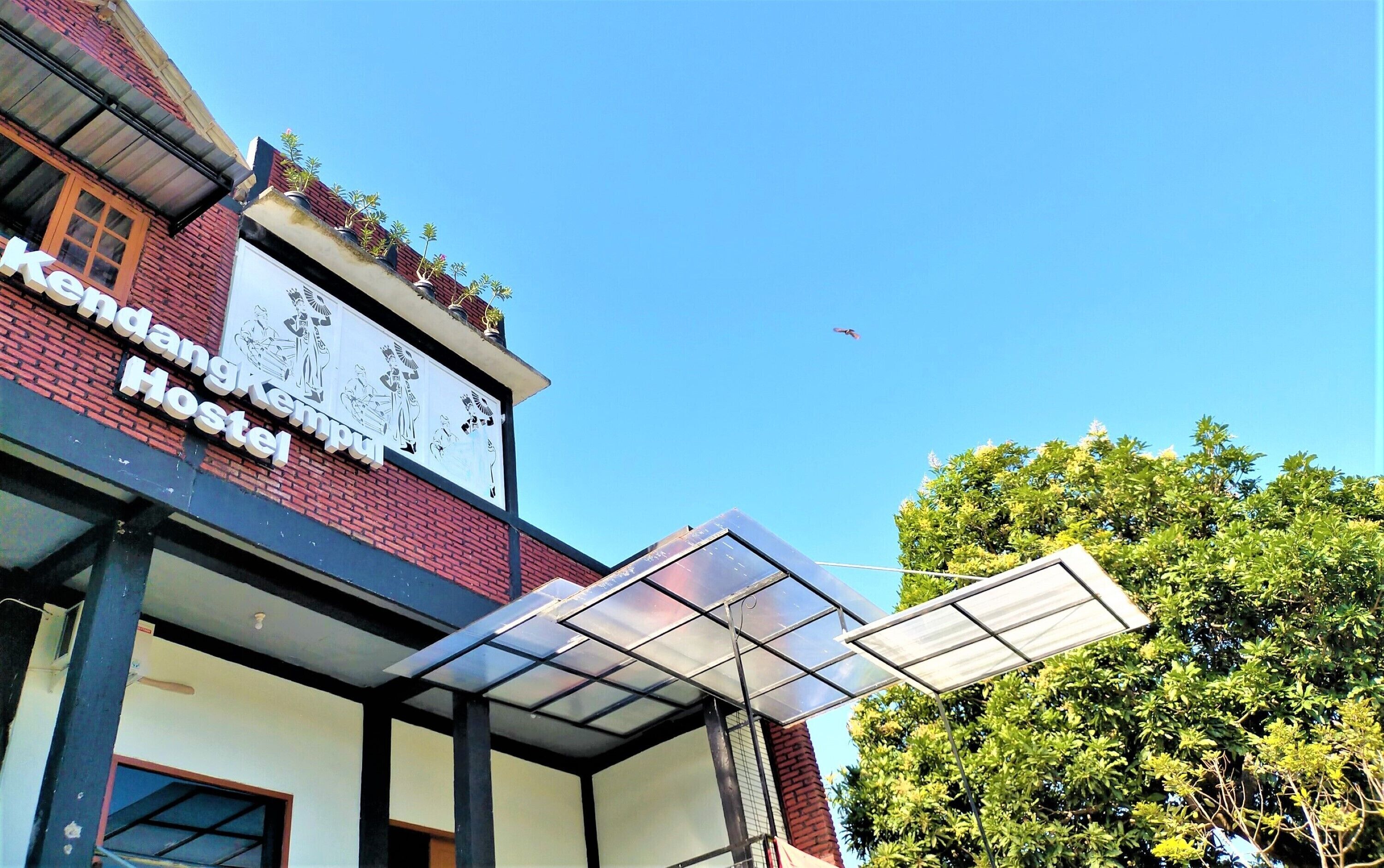 Um hostel com uma placa, estrutura com teto de vidro e céu azul claro.
