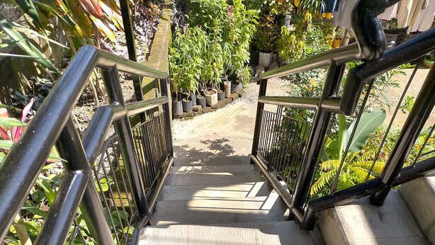 Una escalera de madera con barandales metálicos que conduce a un jardín con macetas.