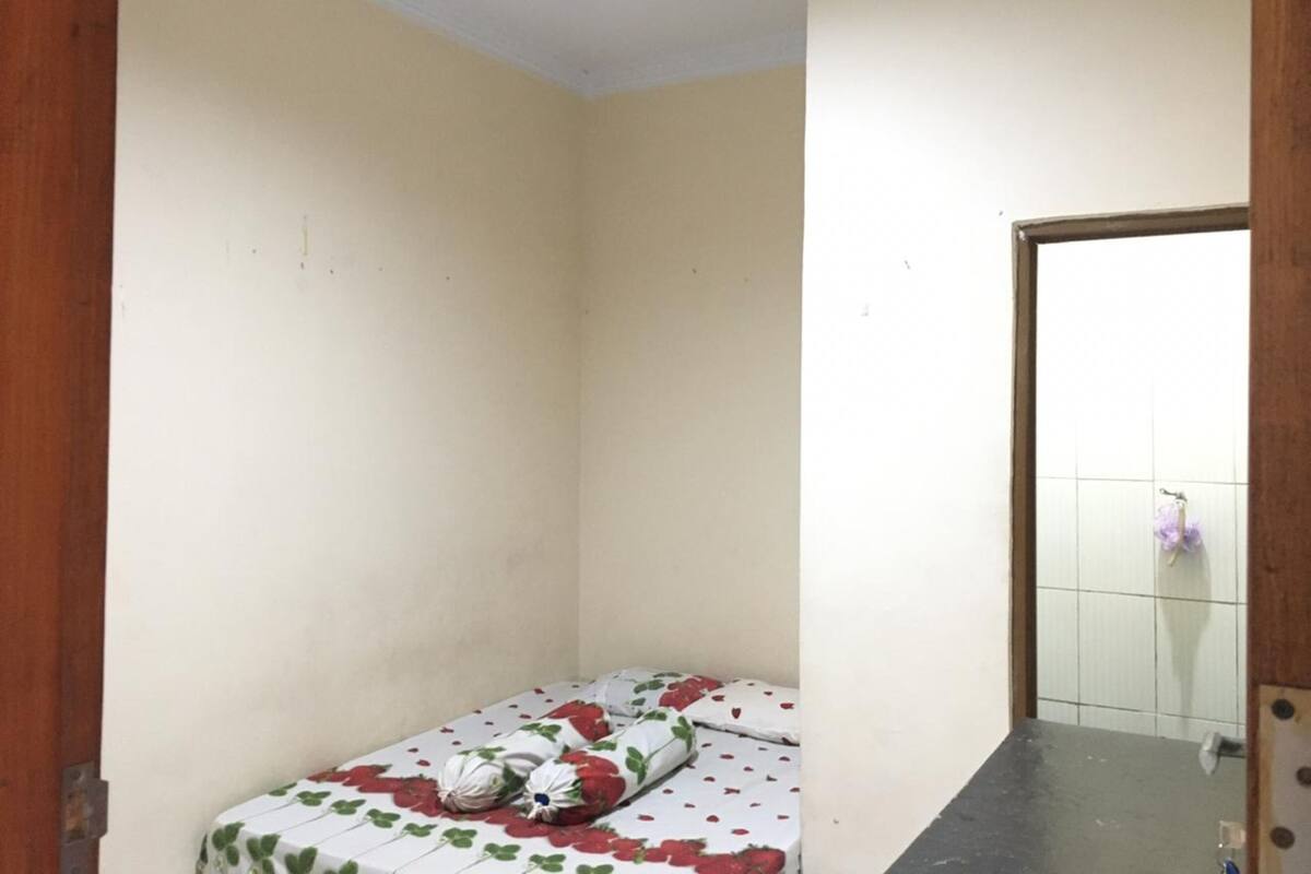 Ein kleines Zimmer mit einem Einzelbett, einem blumigen Bettüberwurf, einer Holztür und einer gefliesten Wand.