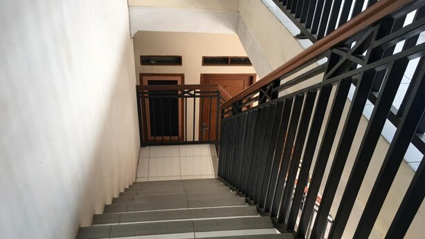Eine Treppe mit hölzernem Geländer und schwarzen Metallhandläufen, die zu einer Zwischenebene mit einer Tür führt.