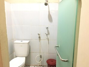 A small bathroom with a toilet, a shower, and a red trash bin.