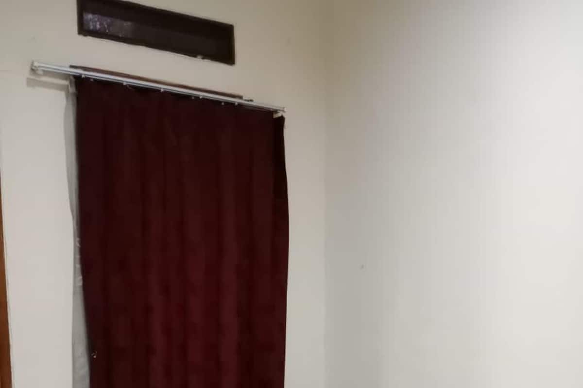 Ein kleines Zimmer mit einem Einzelbett, einer blauen Matratze und einem dunkelroten Vorhang.