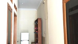 Ein schmaler Flur mit einem weißen Kühlschrank, Holzböden mit Schuhen und einer Tür mit dunklem Rahmen.
