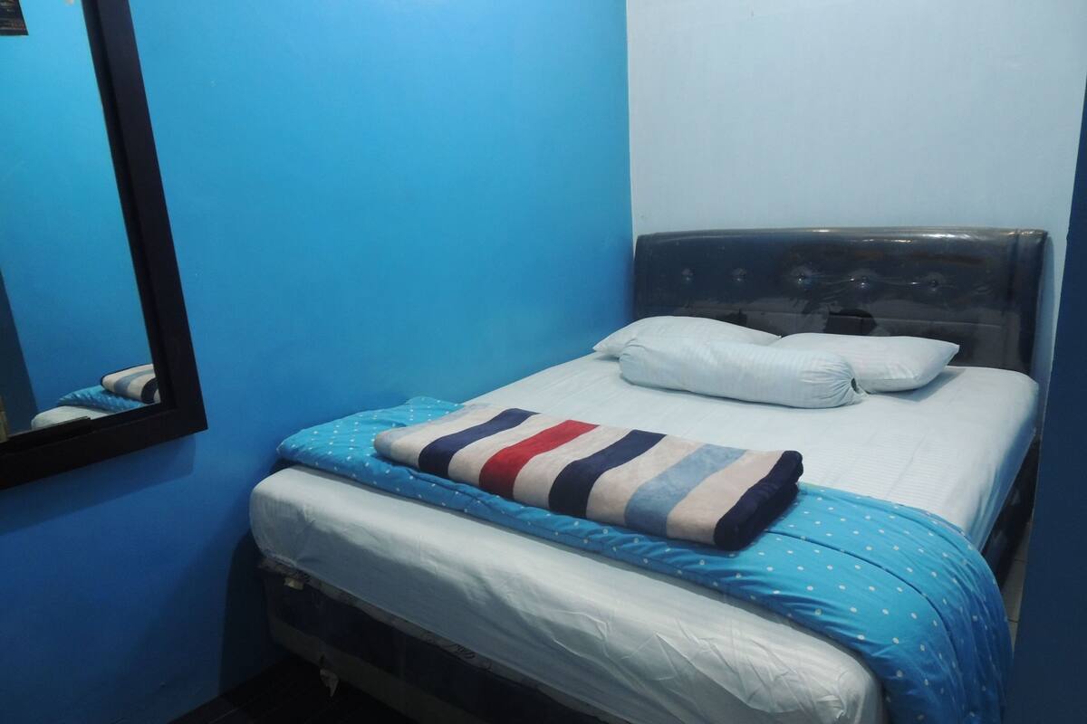 Ein kleines Zimmer mit einem Einzelbett, blauer Wand und einem Spiegel.