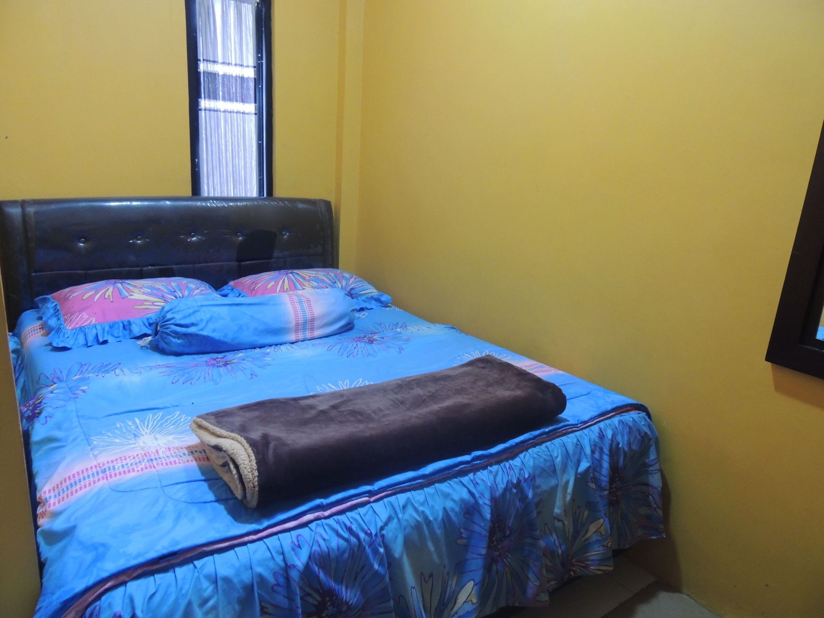 A bed with a blue floral bedspread, two pillows, and a brown blanket.