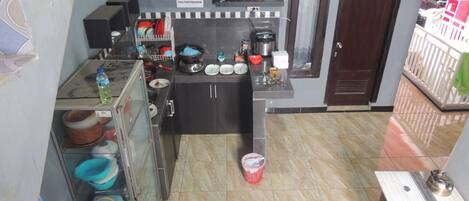 A compact kitchen with a stove, sink, and various kitchen utensils. There are shelves with bottles and a sign indicating a kitchen area.