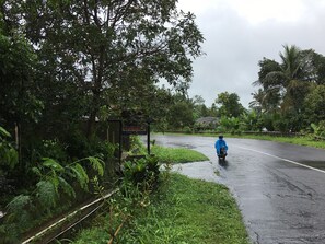 A wet road with a motorcyclist in blue rain gear. - Penginapan Cipto Wening (Pakem)