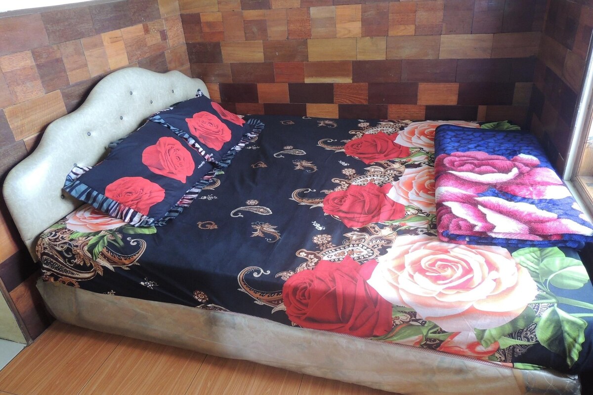 A bed with a floral bedspread, a headboard, and two pillows.