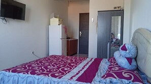 A bedroom with a bed, a wardrobe, a television on the wall, and a door leading to another room.