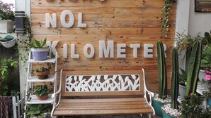 Pared de madera con el texto "DIENG NOL KILOMETER" y un banco delante.