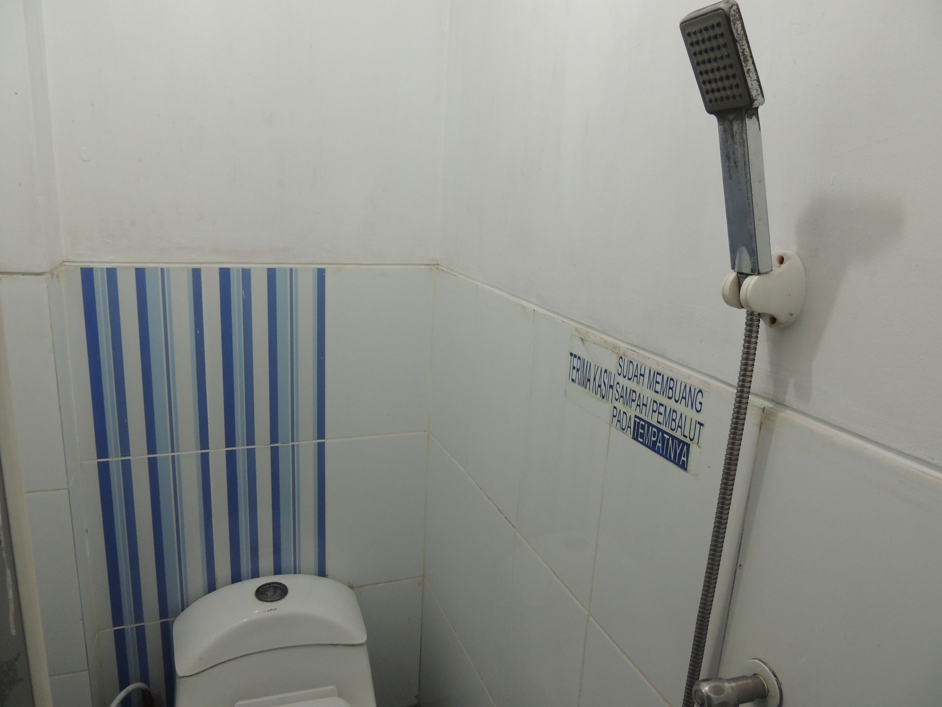 A small bathroom with a shower, a toilet, and a sign on the wall.