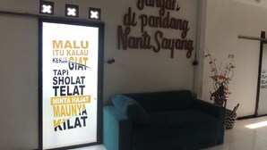 Zona de recepción con un sofá azul, una pared con un cartel en un idioma extranjero y un cuadro enmarcado sobre el sofá.