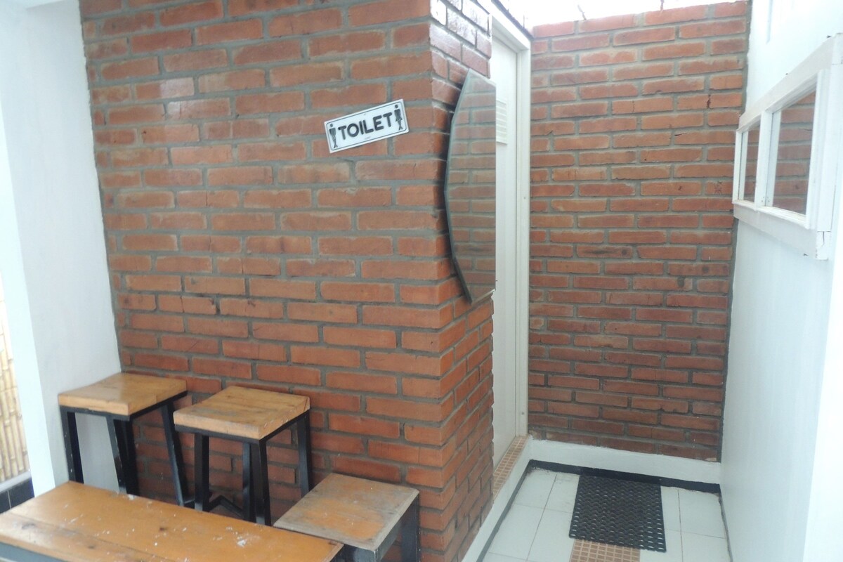 A corner with a brick wall, a sign indicating a toilet, and two wooden tables.