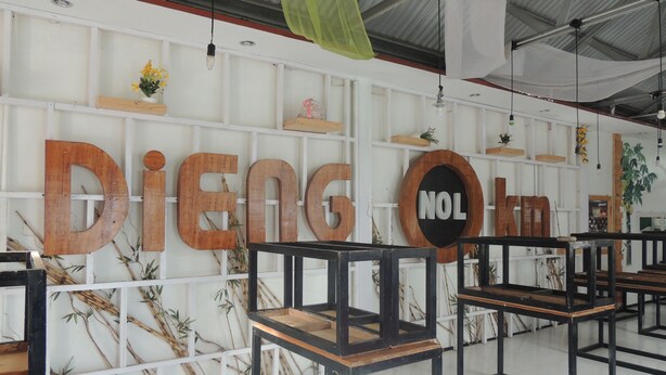 Un interior moderno con letras de madera que deletrean 'DiEng Nol' en la pared, adornos de bambú y muebles minimalistas.