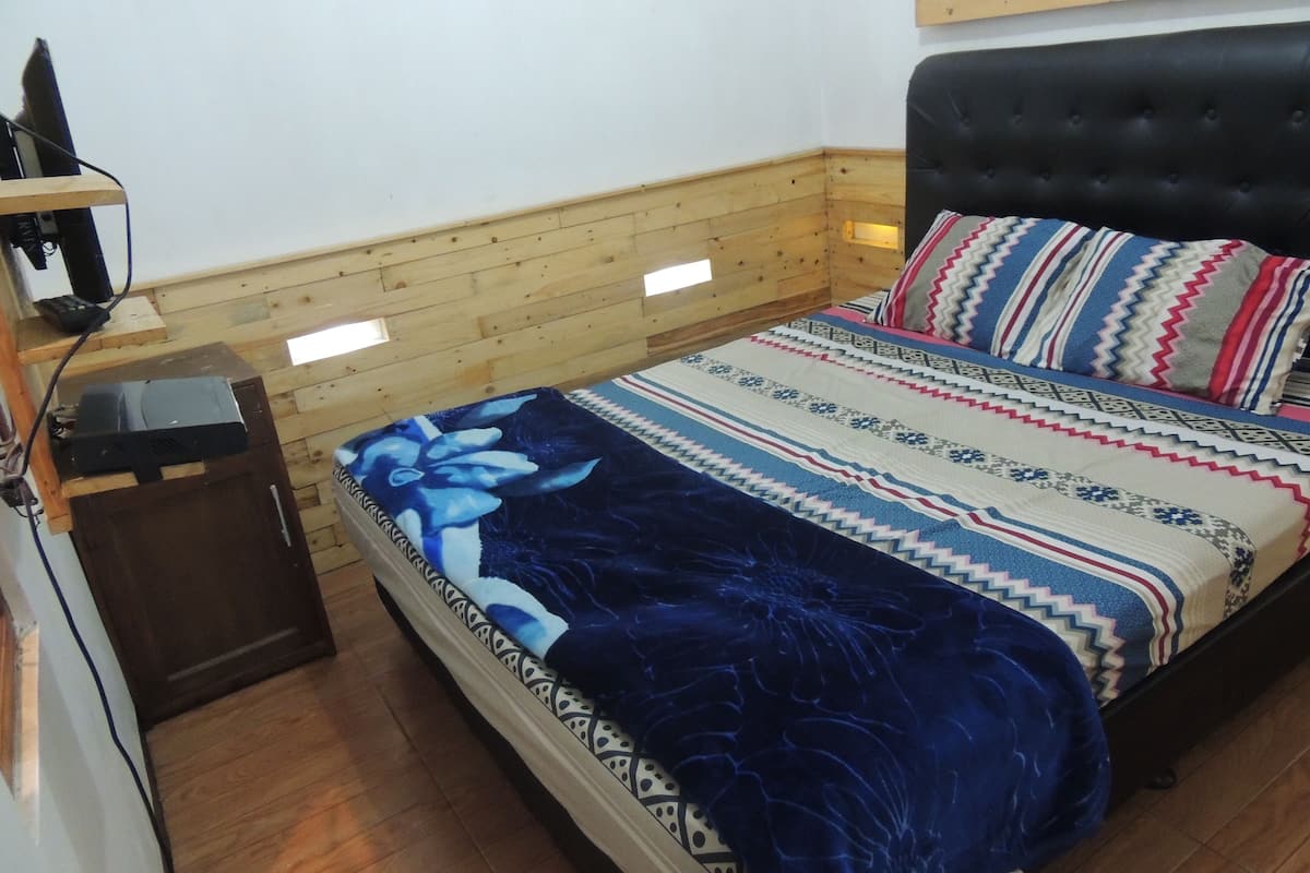 A bedroom with a bed, a wooden headboard, a nightstand, and a wall-mounted shelf.