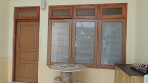 Una habitación con puerta de madera, ventana de múltiples vidrios, una mesa redonda pequeña con taburetes y un armario con una bandeja de objetos.