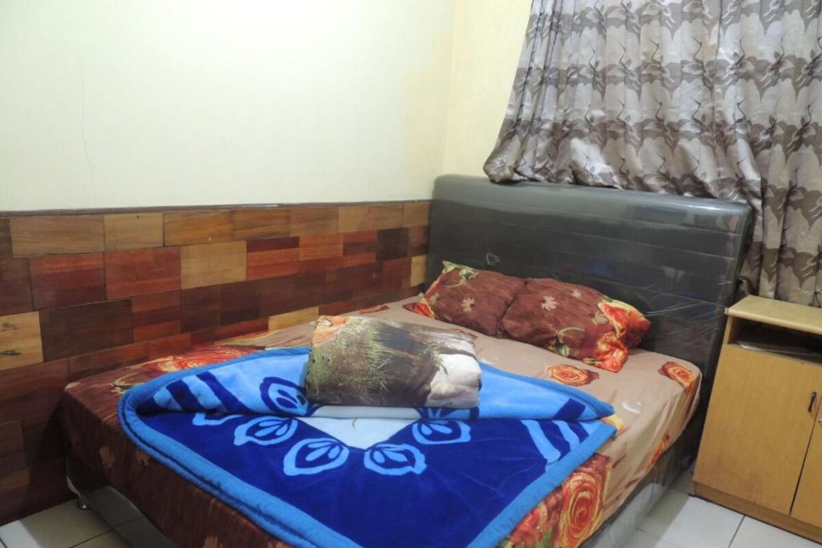 Une chambre à coucher avec un lit, une tête de lit, une armoire en bois et un rideau.