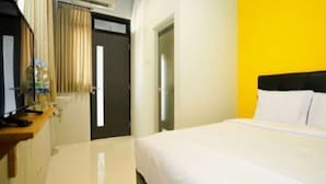 A hotel room with a bed, a desk with a lamp, a mirror, and a door with curtains. - I Cloud Residence (Surabaya)