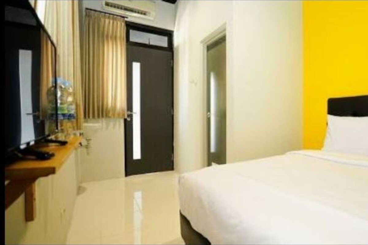 A hotel room with a bed, a desk with a chair, a mirror, and a door.