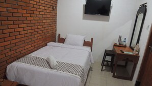 Ein Hotelzimmer mit Backsteinwand, einem Bett mit weißer Bettwäsche, einem Holztisch, einem Stuhl, einem an der Wand befestigten Fernseher und einem Spiegel.