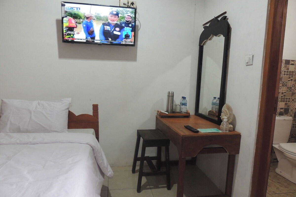 A bedroom with a bed, a desk, a mirror, and a television displaying a news program.