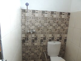 Un baño con baldosas estampadas, un inodoro y una ducha con cabezal de ducha manual.