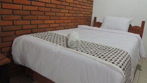 Ein Bett mit weißer Bettwäsche, einer gemusterten Decke, einem Holz-Kopfteil und einer Ziegelwand.