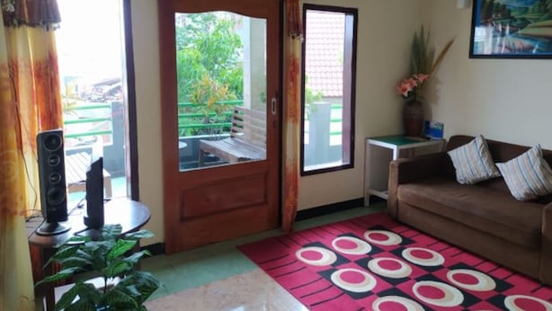 Un salon comprenant un canapé, une table basse, un téléviseur et une porte donnant sur un espace extérieur avec un banc et de la verdure.