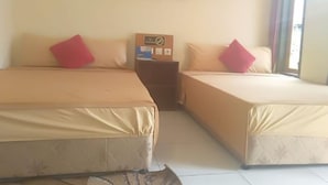 Une chambre d’hôtel avec deux lits, chacun recouvert d’une couvre-lit beige et agrémenté d’un oreiller rouge. On y trouve une petite table sur laquelle est posée une boîte, ainsi qu’un tableau représentant des fleurs accroché au mur.