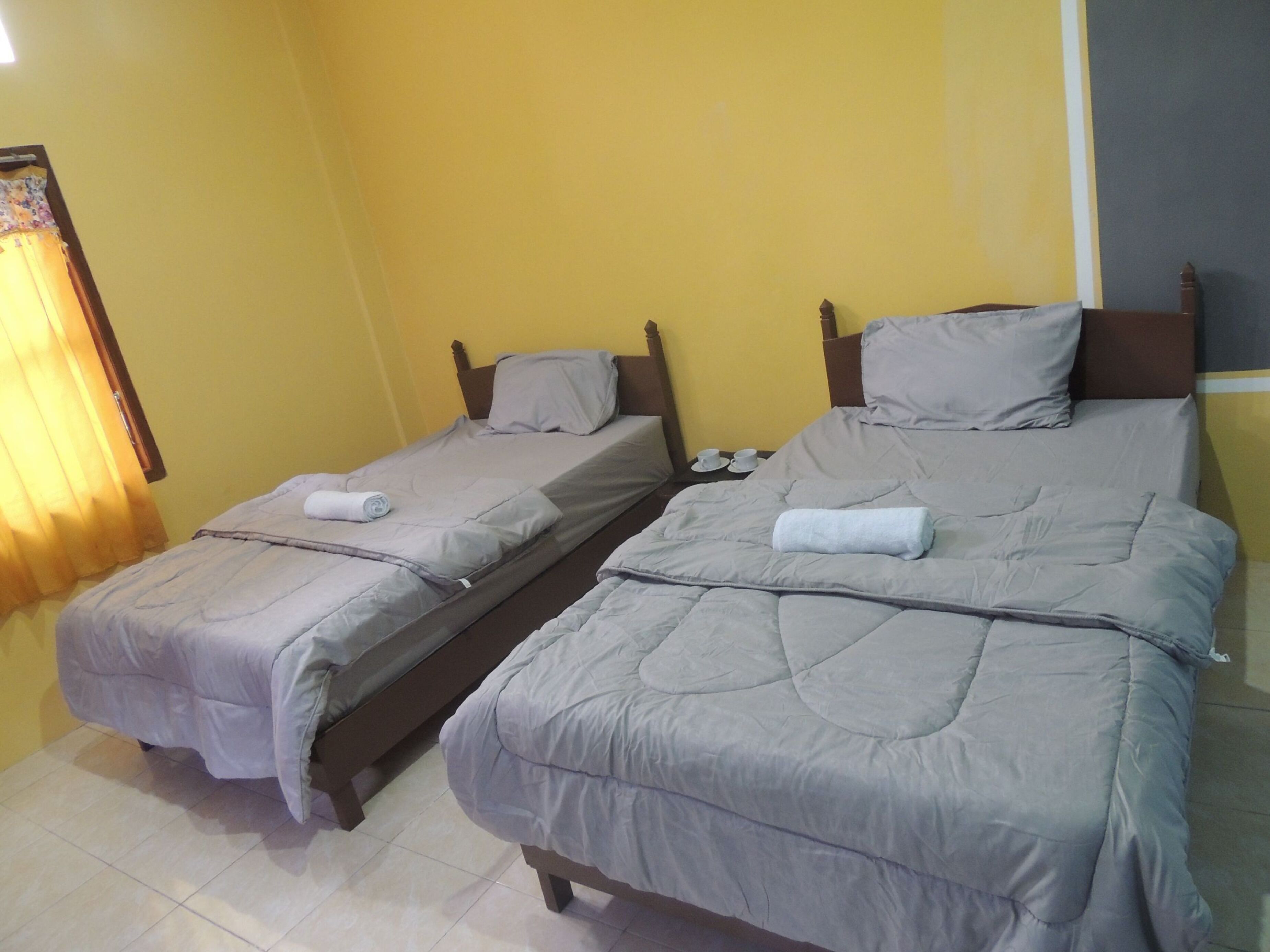 Dos camas individuales con ropa de cama gris y cabeceros de madera en una habitación con paredes amarillas.