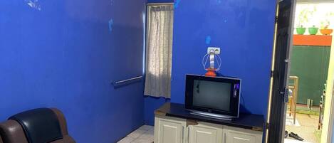 A room with a blue wall, a brown leather sofa, a television on a cabinet, and an air conditioning unit.