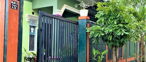 A green house with a black gate, potted plants, and a sign reading "BLOK E 212".