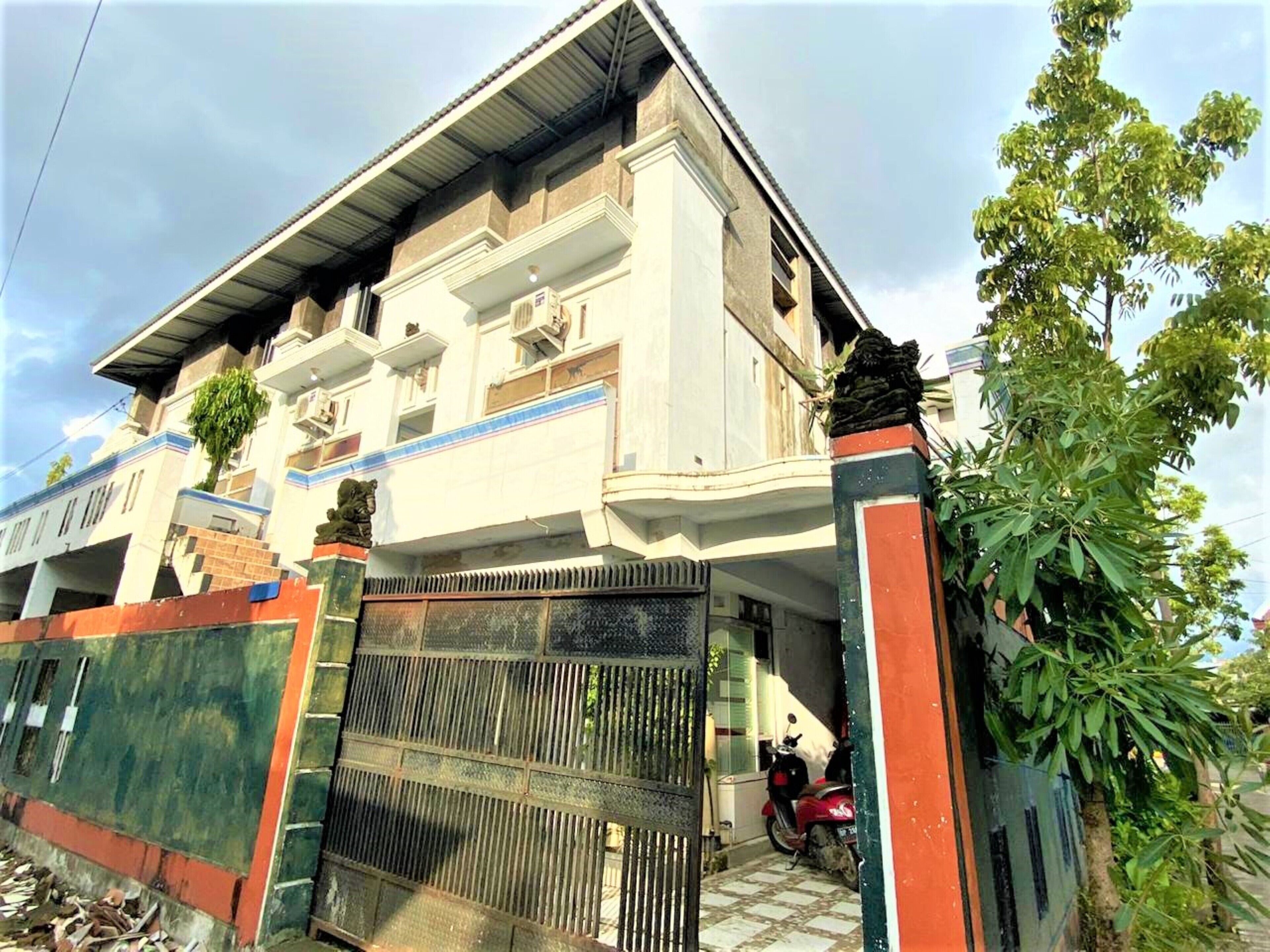 A two-story building with a gated entrance, a red scooter parked inside, and a tree to the right.
