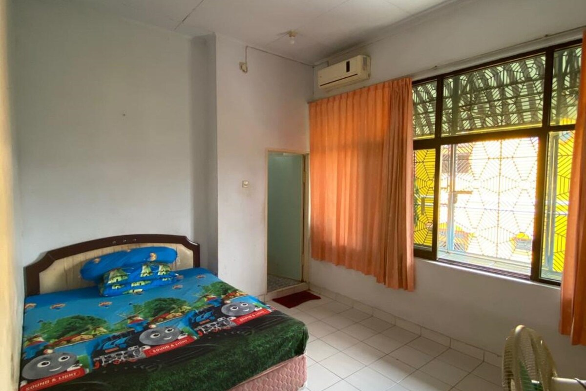 Een slaapkamer met een bed, een raam met gordijnen, een ventilator en een airconditioning.
