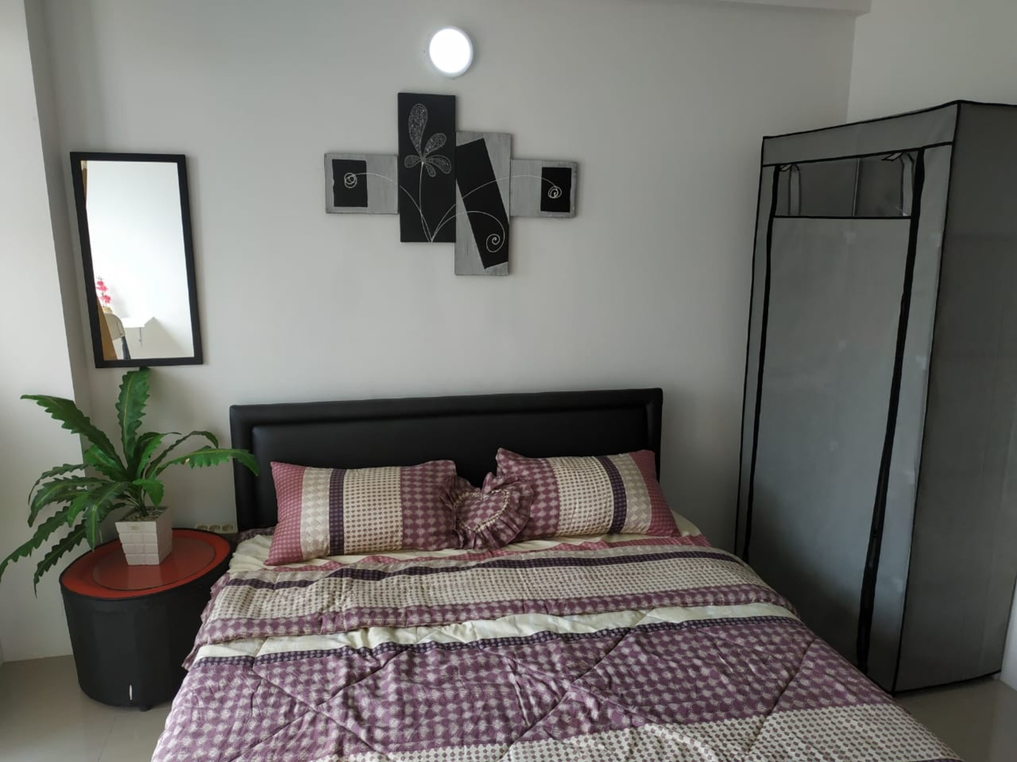 Un dormitorio con cama, planta en maceta, espejo, decoración en la pared y armario.