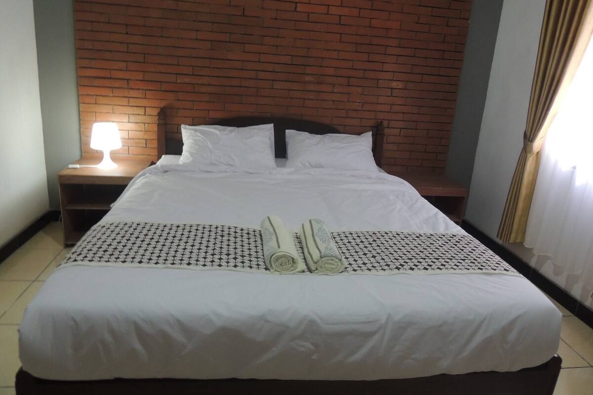 A neatly made bed with white linens, a wooden headboard, and a nightstand with a lamp.