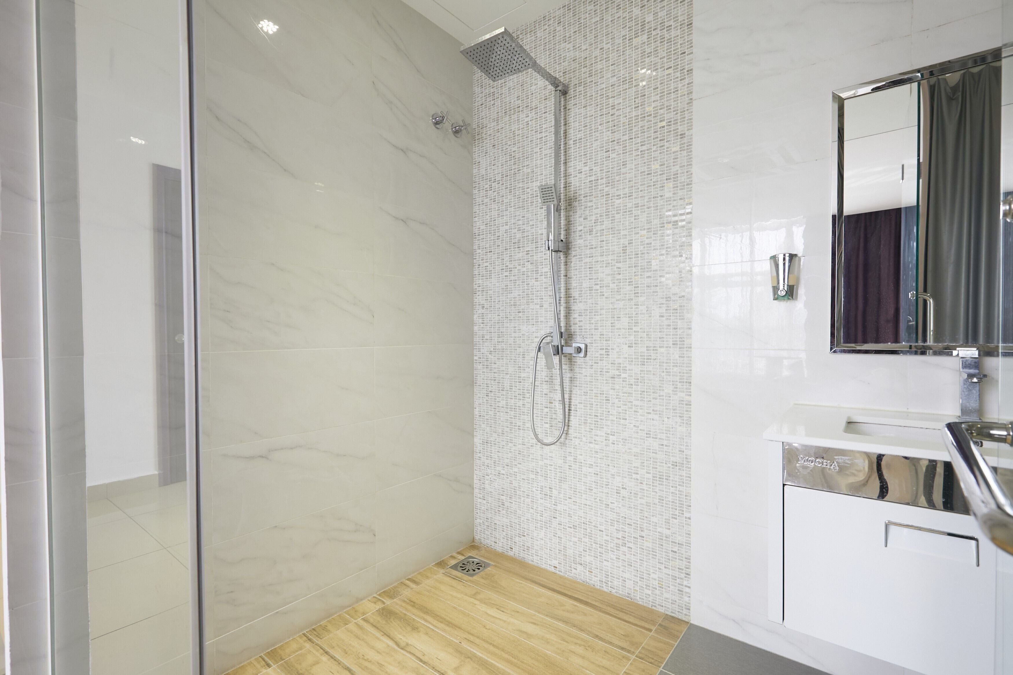 Un baño moderno con cabina de ducha de vidrio, suelo de madera y pared de azulejos blancos con un diseño en mosaico.