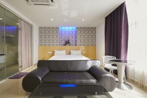 Una habitación de hotel moderna con una cama grande, un sofá de cuero negro, una pequeña mesa redonda y un box de ducha de vidrio.