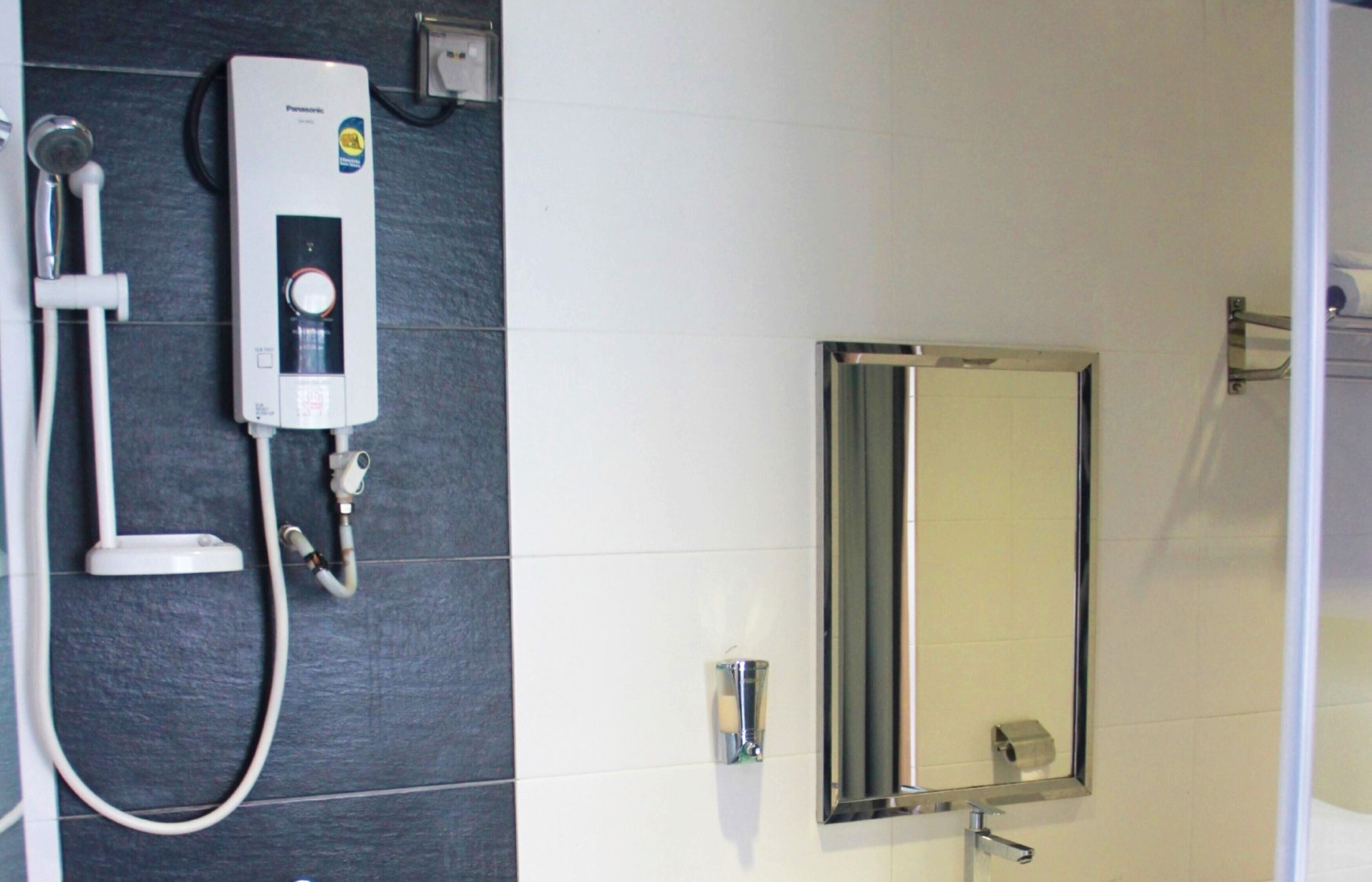 A bathroom with a wall-mounted water heater, a handheld showerhead, and a mirror.