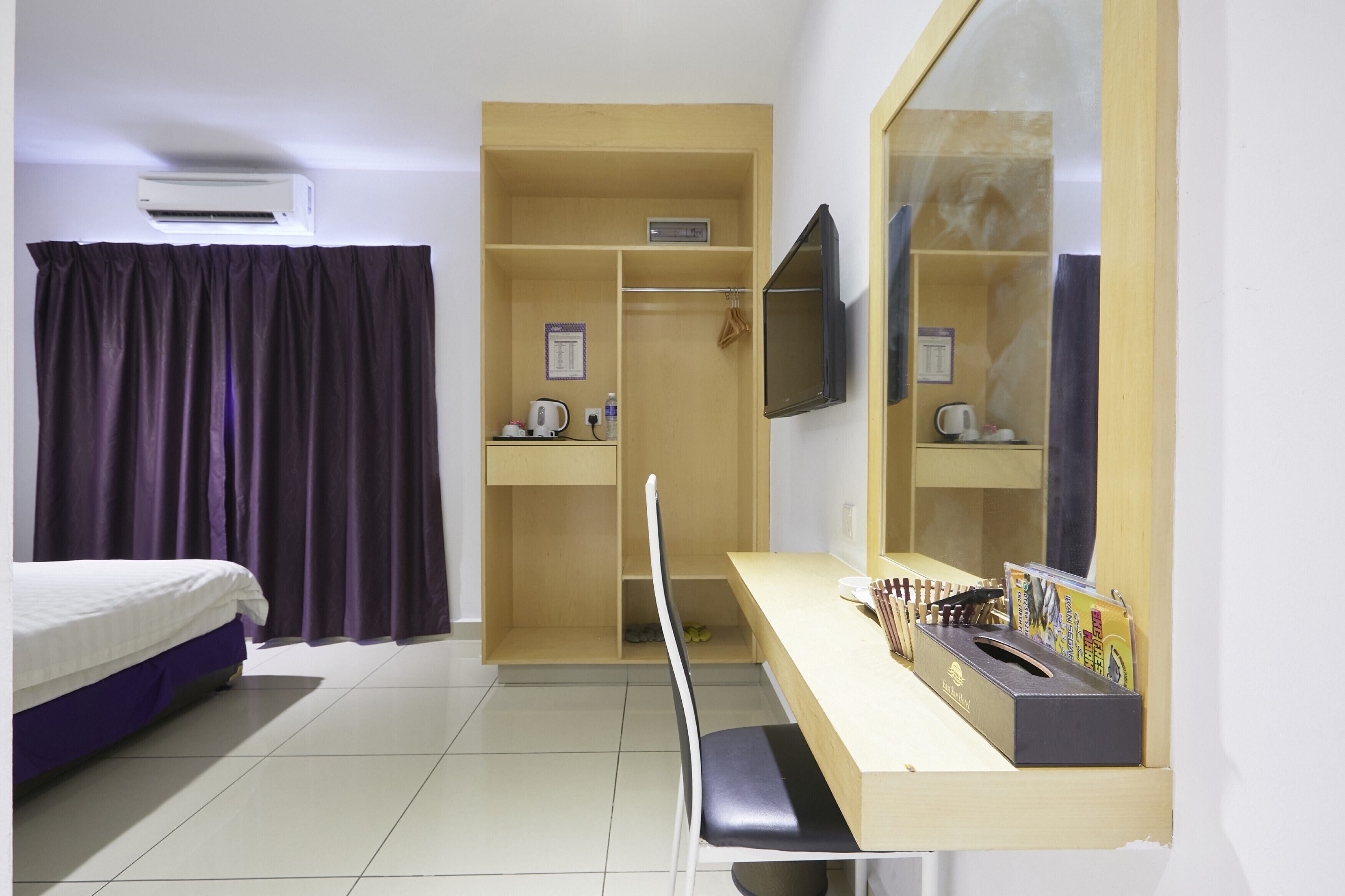 Una habitación de hotel con cama, escritorio con espejo, armario y televisor montado en la pared.