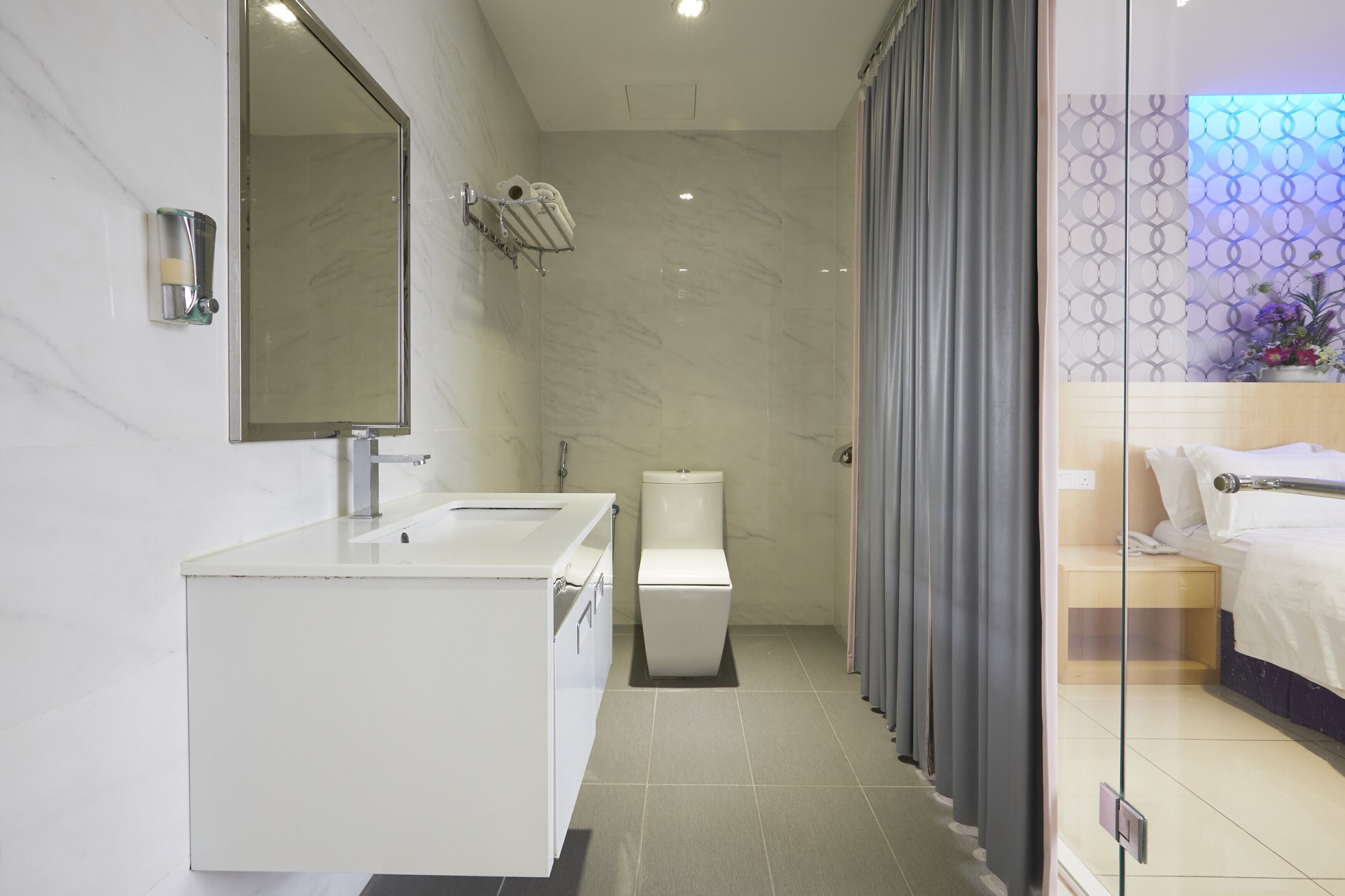 A modern bathroom with a large mirror, a white sink, a toilet, and a shower area.