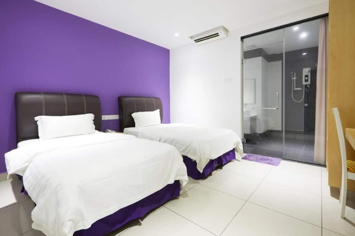 A hotel room with two beds, a shower area, and a purple wall.