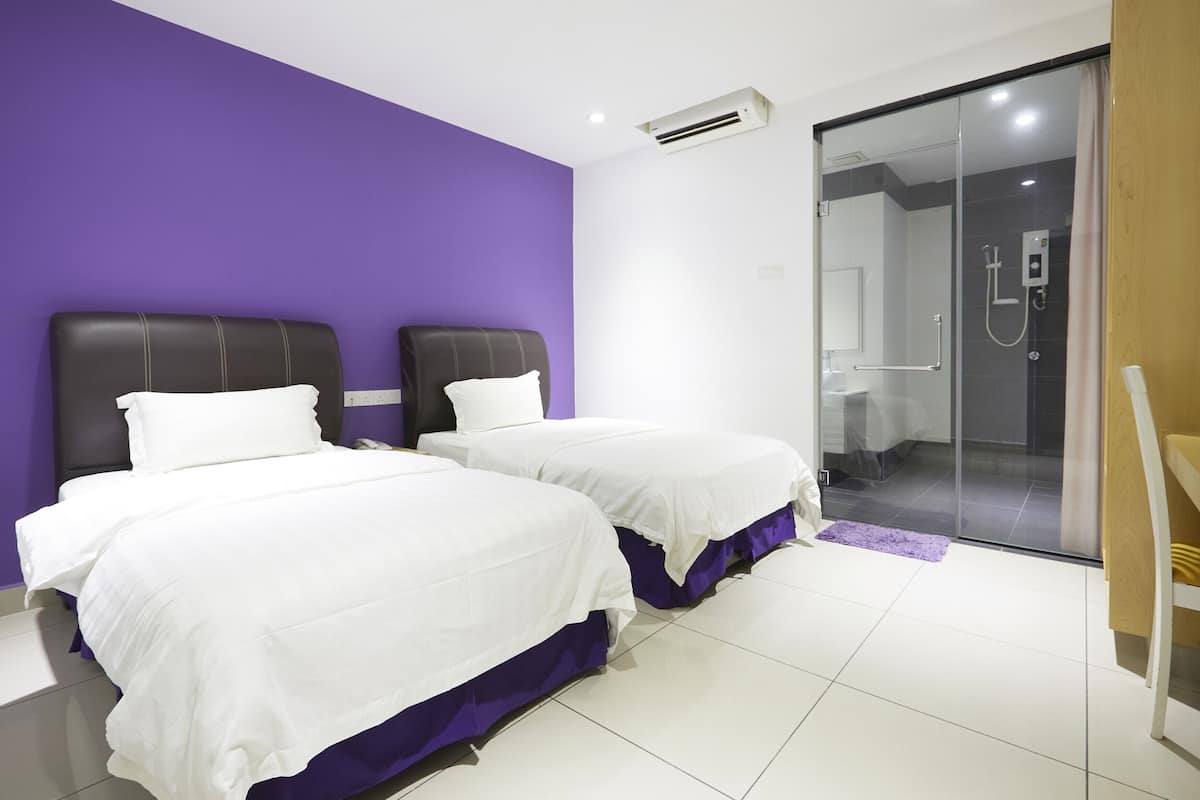 A hotel room with two beds, a shower area, and a wooden chair.