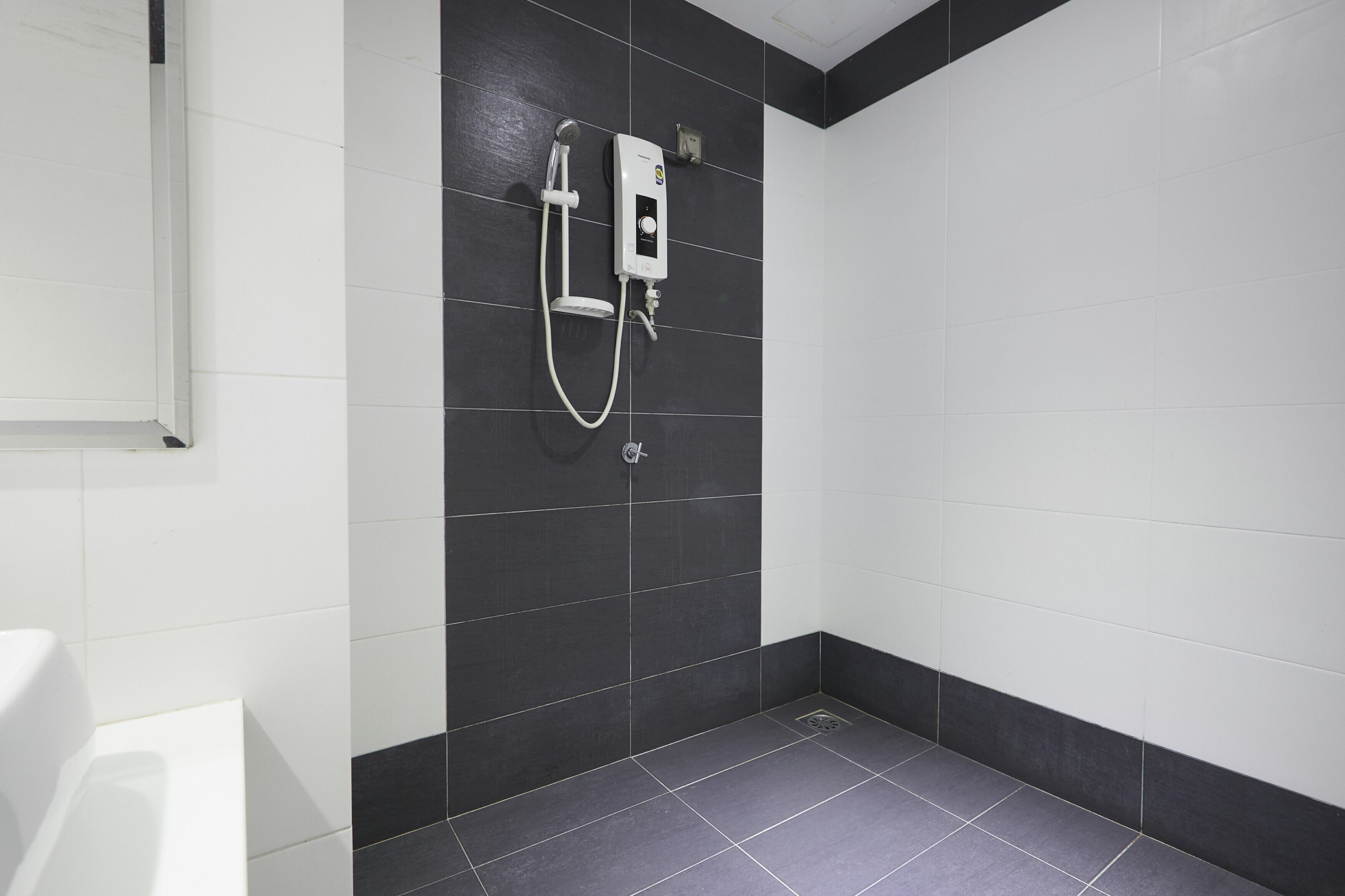 A modern bathroom with a black and white tiled wall, a white sink, and a shower unit.