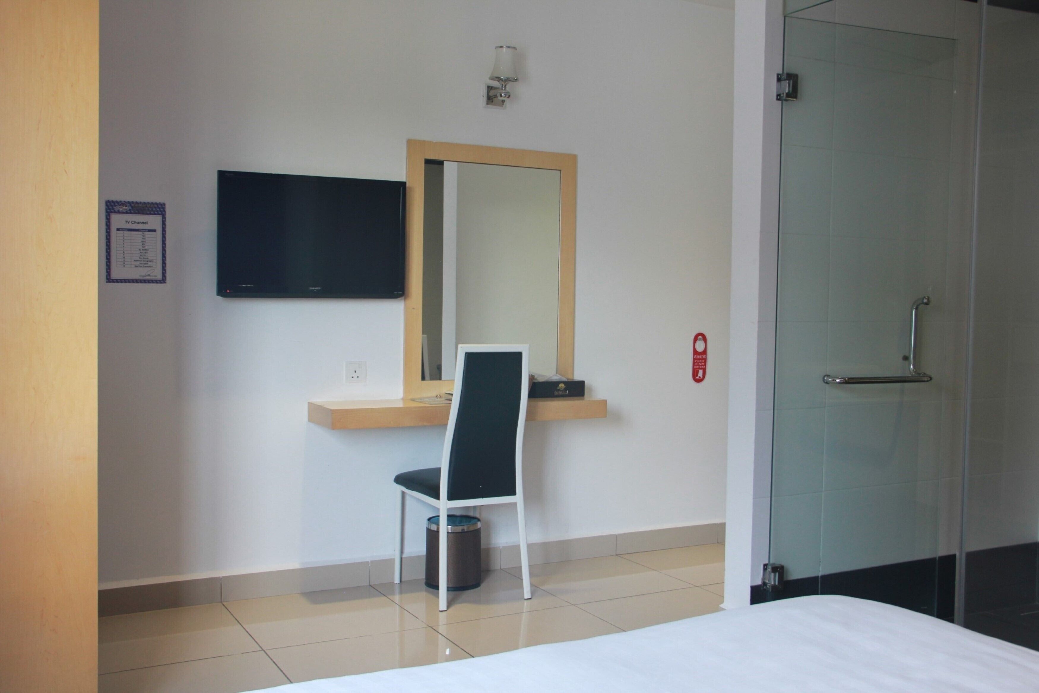 Een hotelkamer met een bed, een bureau met stoel, een aan de muur bevestigde televisie, een spiegel en een douchecabine met glazen deur.