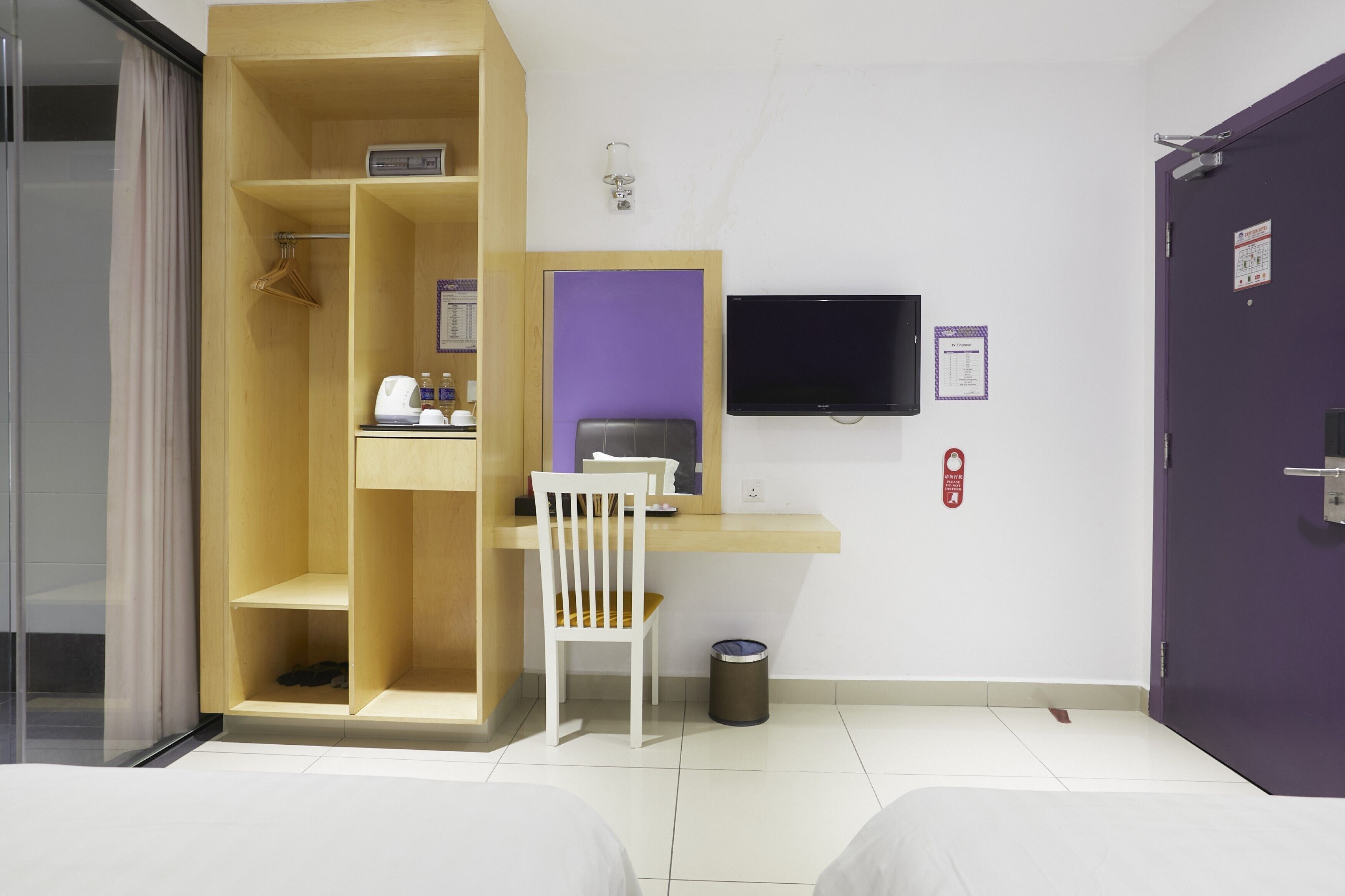 Quarto de hotel com cama, escrivaninha, cadeira, televisão e guarda-roupa.