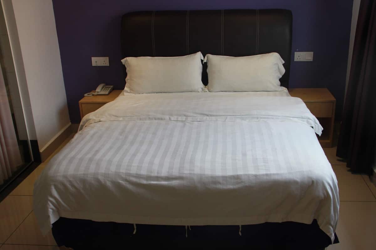 A neatly made bed with a striped bedspread, two pillows, and a bedside table with a telephone.